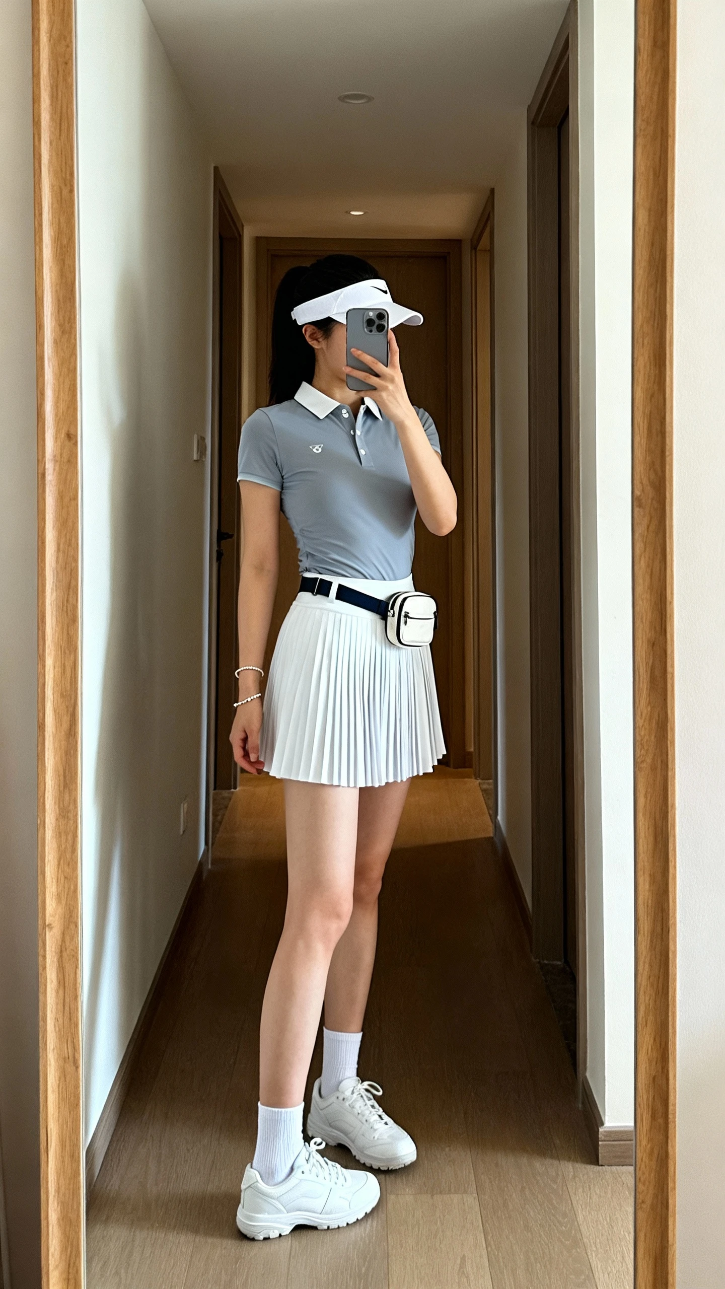 iPhone back view of a woman wearing a sporty pleated skort with a fitted polo top, visor, white court sneakers, ankle socks, a small belt bag, and a delicate tennis bracelet, face not visible, hallway full-length mirror, indoor lighting, iPhone photo quality.