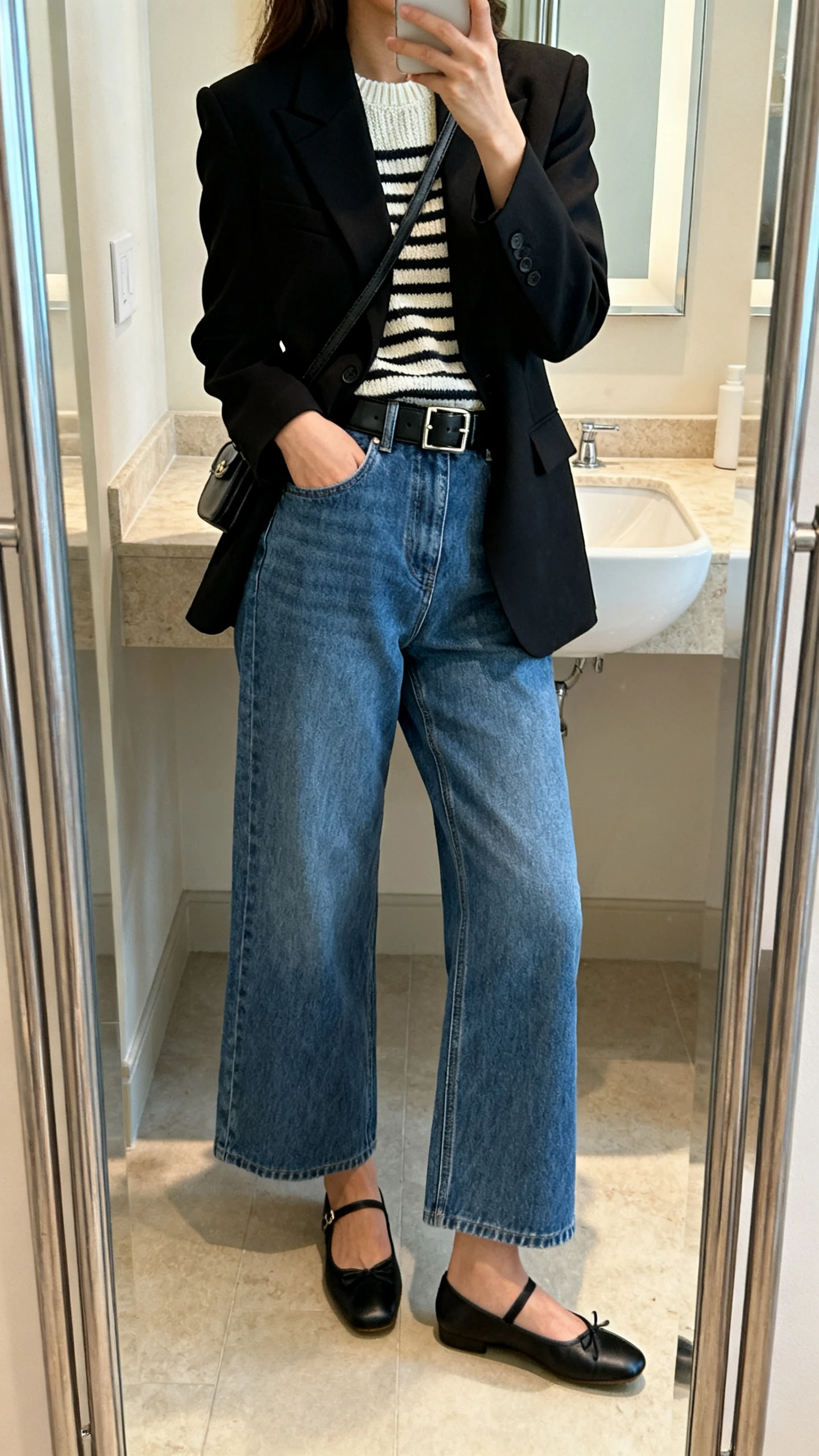 iPhone side-angle mirror selfie of a woman in a black Parisian-style blazer, classic blue high-waisted denim, striped knit underlayer, black leather belt, ballet flats, and a small crossbody, face not visible, bathroom mirror, soft indoor lighting, iPhone photo quality